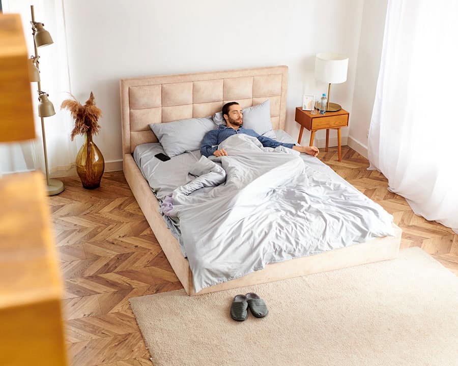 man sleeping on his back in bed, inside his room