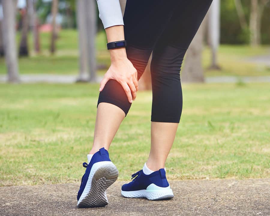Woman runner hold her sports injured leg behind her knee