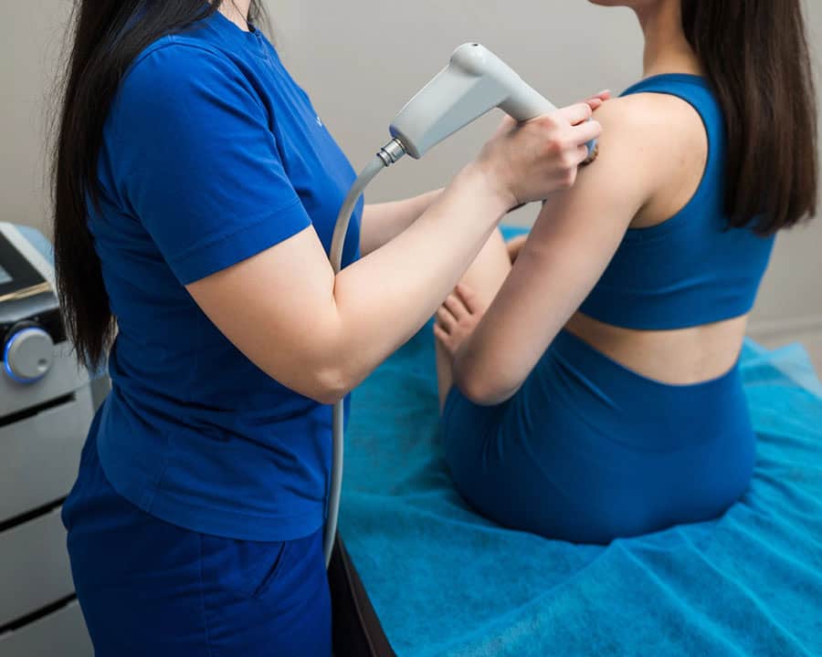 physiotherapist applying shockwave therapy to a female patient's shoulder