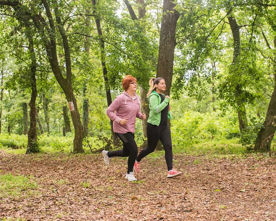 Mother and daughter wearing sportswear and running in green forest during spring
